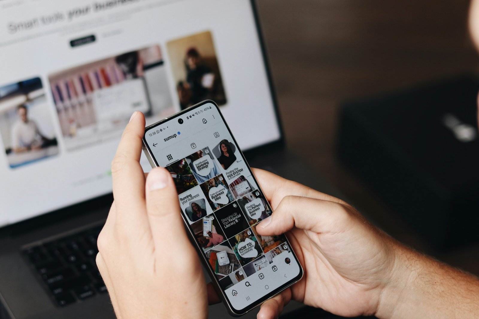 A person holding a cell phone in front of a laptop